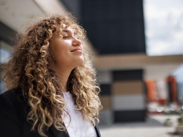 20 Foods That Boost NAD Levels 6 A woman with voluminous curly hair tilts her head back with eyes closed, appearing peaceful in bright natural lighting.Retry