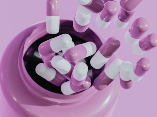 NAD Levels by Age Group: What's Considered Normal? 14 Pink and white capsules spill from a dark circular container onto a matching pink surface.