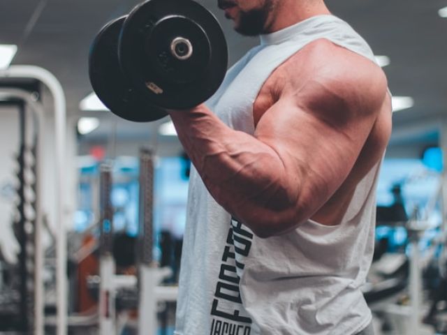 How Creatine Became an Anti-Aging and Longevity Essential 6 Man in white tank top lifting a black dumbbell.